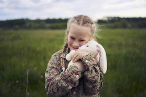 een mooi blond meisje met haar speelgoed- konijn is spelen in de veld- foto