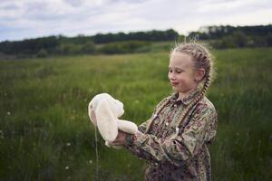 een mooi blond meisje met haar speelgoed- konijn is spelen in de veld- foto