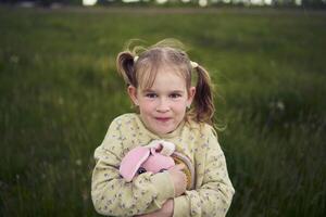 een mooi blond meisje met haar speelgoed- konijn is spelen in de veld- foto