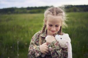 een mooi blond meisje met haar speelgoed- konijn is spelen in de veld- foto