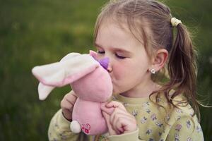 een mooi blond meisje met haar speelgoed- konijn is spelen in de veld- foto