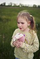 een mooi blond meisje met haar speelgoed- konijn is spelen in de veld- foto