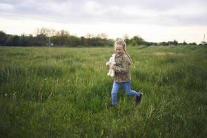 een mooi blond meisje met haar speelgoed- konijn is spelen in de veld- foto