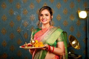 afbeelding van een jong, glimlachen model- in traditioneel Indisch kleding glimlachen en Holding een puja bord gedurende de viering van diwali foto