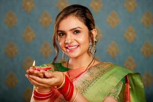 een aantrekkelijk Indisch huisvrouw poses voor de camera terwijl Holding een diya en grijnzend Bij de festival van diwali terwijl aandoen een traditioneel Saree foto