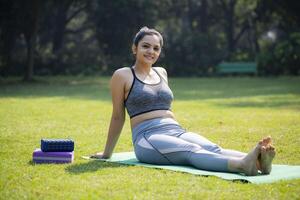 vrouw yoga leraar is zittend in de park met haar armen en poten uitgestrekt foto