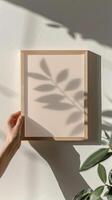 een mockup van een minimalistisch a4 kader een vrouw hand- Holding de houten a4 kader zichtbaar Deens pastel esthetisch in de kamer foto