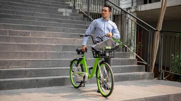 een gefocust Aziatisch zakenman voortvarend een groen fiets in de stad, gaan naar werk met zijn fiets. foto