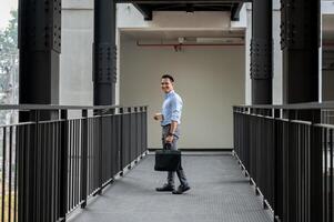 een zelfverzekerd, ervaren Aziatisch millennial zakenman staat Aan een bedrijf gebouw hal. foto