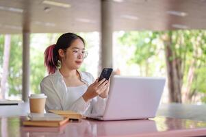 een vrouw college leerling gebruik makend van haar smartphone terwijl zittend Bij een tafel in een campus cafetaria. foto