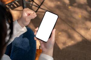 een vrouw tonen een gebalde vuist terwijl gebruik makend van haar telefoon buitenshuis, presentatie van een wit scherm model. foto