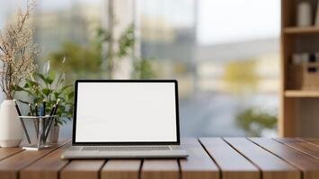 een voorkant visie van een laptop computer mockup en decoratief voorwerpen zijn Aan een houten tafelblad in een kamer. foto