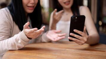 twee gelukkig Aziatisch vrouw vrienden genieten van aan het kijken iets Aan een telefoon en pratend Bij een restaurant. foto