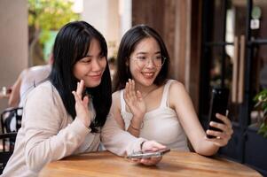 twee gelukkig jong Aziatisch vrouw vrienden zijn pratend Aan een telefoontje met hun vrienden Bij een restaurant. foto