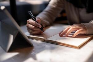 een bijgesneden beeld van een vrouw college leerling nemen aantekeningen terwijl aan het studeren online Aan haar tablet. foto