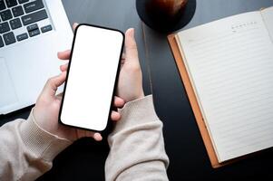 top visie beeld van een vrouw hand- Holding een wit scherm smartphone mockup over- een modern kantoor bureau. foto