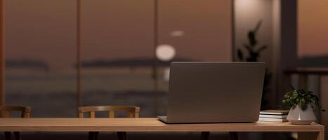 een laptop Aan een tafel in een modern kamer met een verbazingwekkend groot glas venster met een oceaan visie Bij zonsondergang foto