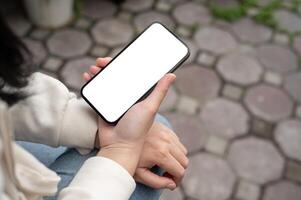 een detailopname beeld van een vrouw lezing of aan het kijken videos Aan haar smartphone terwijl zittend buitenshuis. foto