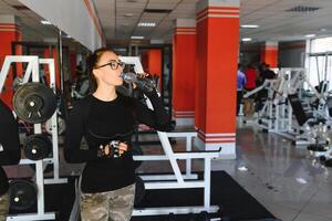 jong vrouw drinken water na oefenen. geschiktheid Sportschool foto