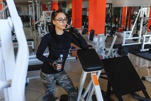 professioneel bodybuilding atleet kom tot rust na vermoeiend opleiding. atleet kom tot rust en drinken water van sport fles in Sportschool interieur foto