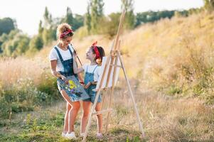 jong aantrekkelijk moeder geeft les dochter schilderij in zomer park. buitenshuis werkzaamheid voor school- leeftijd kinderen concept. foto