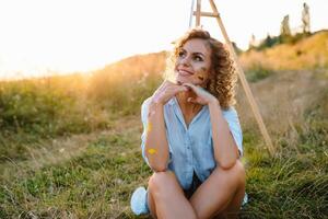 mooi vrouw is schilderen. Open lucht sessie. schattig vrouw trekt een afbeelding Bij zonsondergang. meisje artiest. foto