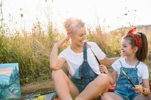 moeder geeft les dochter verf in park. zonnig natuur, mam en dochter verf een afbeelding in een park , schilderij een weinig kind, kind creativiteit. moeder dag. foto