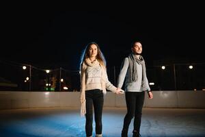 winter schaatsen, liefhebbend paar Holding handen en rollend Aan baan. verlichting in achtergrond, nacht. concept opleiding. foto