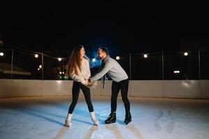 winter schaatsen, liefhebbend paar Holding handen en rollend Aan baan. verlichting in achtergrond, nacht. concept opleiding. foto