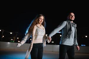 winter schaatsen, liefhebbend paar Holding handen en rollend Aan baan. verlichting in achtergrond, nacht. concept opleiding. foto