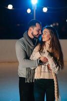 thema ijs het schaatsen baan en liefhebbend paar. vergadering jong, elegant mensen rijden door hand- in menigte Aan stad het schaatsen baan lit door licht bollen en lichten. ijs het schaatsen in winter voor Kerstmis Aan ijs arena. foto