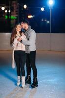 thema ijs het schaatsen baan en liefhebbend paar. vergadering jong, elegant mensen rijden door hand- in menigte Aan stad het schaatsen baan lit door licht bollen en lichten. ijs het schaatsen in winter voor Kerstmis Aan ijs arena. foto