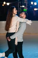 thema ijs het schaatsen baan en liefhebbend paar. vergadering jong, elegant mensen rijden door hand- in menigte Aan stad het schaatsen baan lit door licht bollen en lichten. ijs het schaatsen in winter voor Kerstmis Aan ijs arena. foto