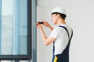 werkman in overall installeren of aanpassen plastic ramen in de leven kamer Bij huis foto