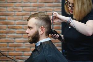 elegant Mens zittend kapper winkel haar stylist kapper vrouw snijdend zijn haar- portret knap gelukkig jong gebaard Kaukasisch vent krijgen modieus kapsel aantrekkelijk kapper meisje werken portie cliënt. foto