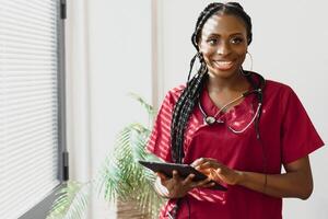 portret van glimlachen vrouw dokter vervelend scrubs in ziekenhuis gang Holding digitaal tablet. foto