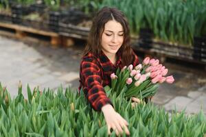 mooi jong glimlachen meisje, arbeider met bloemen in serre. concept werk in de serre, bloemen, tulpen, doos met bloemen. kopiëren ruimte. foto