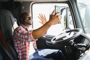 vrachtauto bestuurder telefoontje Aan smartphone in cockpit. vrachtwagenchauffeur Aziatisch jong Mens baard geparkeerd voor koffie breken na lang drijfveer. arbeider mannetje het rijden semi-vrachtwagen vervoer logistiek uitdrukken levering Diensten. foto