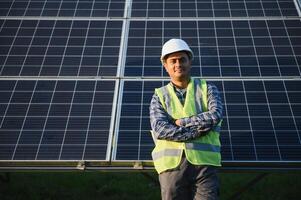 Indisch Mens in uniform Aan zonne- boerderij. bekwaam energie ingenieur controlerend werk van fotovoltaïsche cellen foto