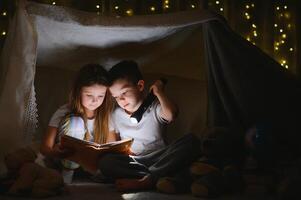 weinig kinderen erbij betrekken in lezing verbazingwekkend boek. ze aan het liegen in mooi hoor speelgoed- tent in speelkamer. jongen Holding zaklamp in hand- foto