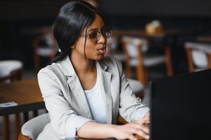 gefocust jong Afrikaanse Amerikaans zakenvrouw of leerling op zoek Bij laptop, echt zwart vrouw werken of aan het studeren met computer aan het doen Onderzoek of voorbereidingen treffen voor tentamen online foto