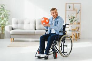 gehandicapt Mens in rolstoel Holding bal met droefheid, kan niet Speel spel, gevoel depressief Bij huis. foto