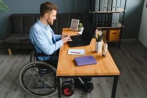 gehandicapten zakenman zittend Aan rolstoel en gebruik makend van computer in kantoor foto