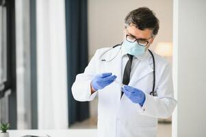 midden oud mannetje dokter vervelend beschermend masker Holding een injectiespuit met vaccin. foto