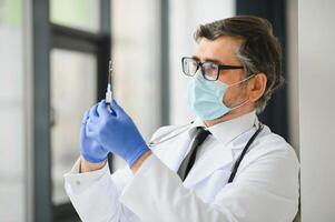 midden oud mannetje dokter vervelend beschermend masker Holding een injectiespuit met vaccin. foto