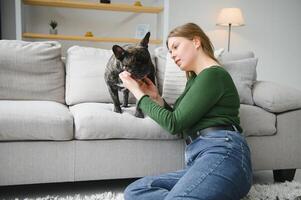 mooi meisje, glimlachen en zittend Aan verdieping in de buurt Frans bulldog foto