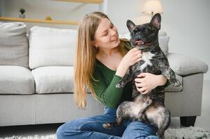 mooi meisje, glimlachen en zittend Aan verdieping in de buurt Frans bulldog foto