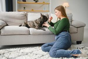 mooi meisje, glimlachen en zittend Aan verdieping in de buurt Frans bulldog foto