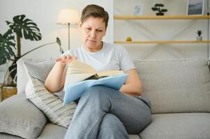 vrouw in huis zittend Aan sofa lezing boek. foto