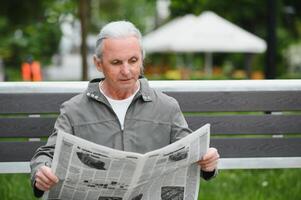 portret van senior Mens lezing Aan bank gedurende zomer dag. foto